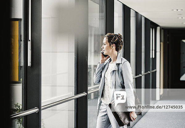 Businesswoman on cell phone looking out of window in office passageway