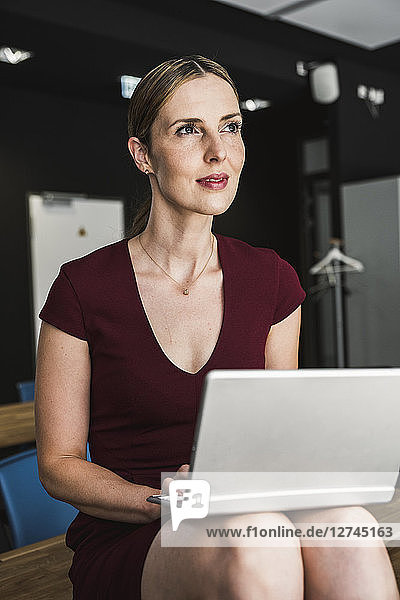Businesswoman in office wearing burgundy dress using laptop