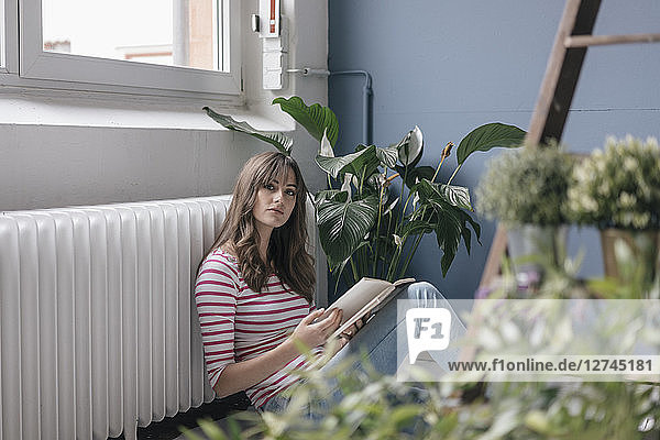 Woman sitting on ground in her new home  reading a book  surrounded by plants