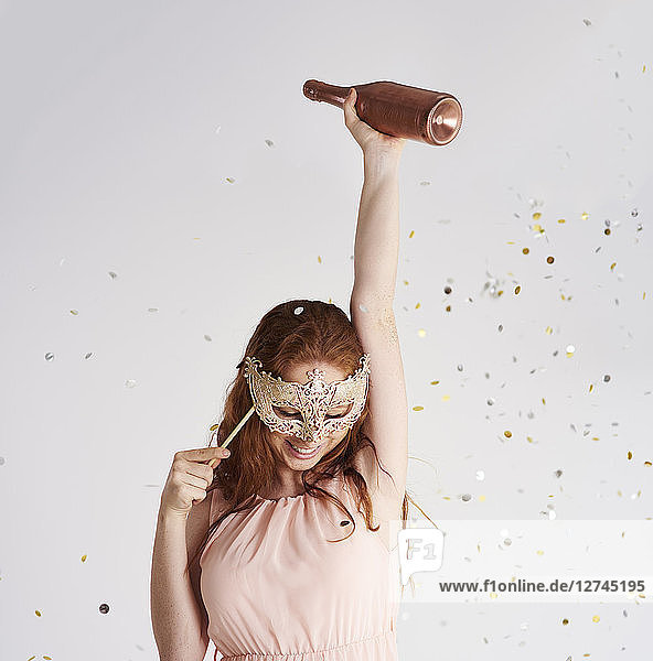 Happy young woman with bottle of champagne and masquerade mask