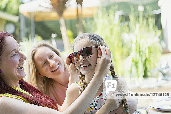 Lesbian couple and daughter playing with sunglasses on patio