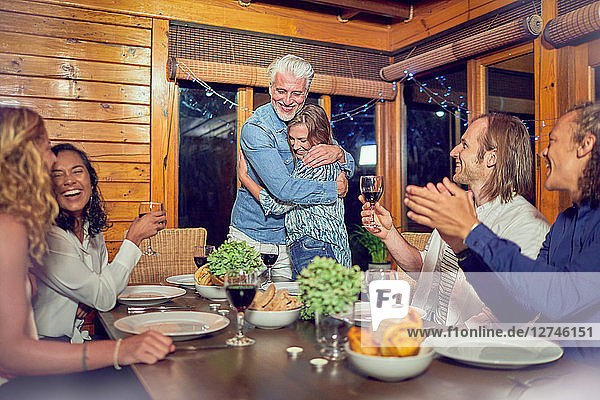 Friends clapping for affectionate couple hugging at dinner table