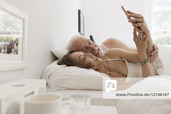 Affectionate senior couple using smart phone in bed