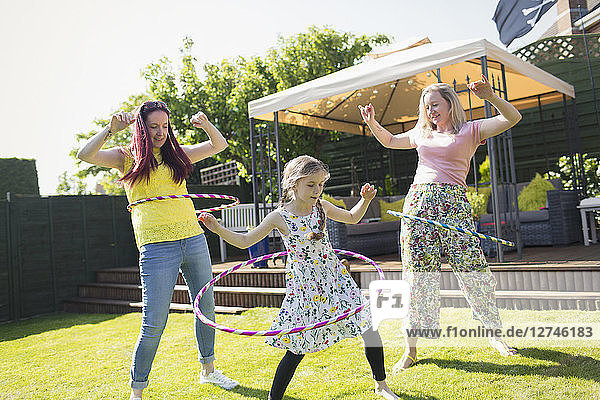 Lesbian couple and daughter playing with plastic hoops in sunny backyard