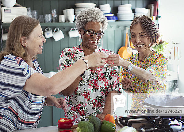 Active senior women friends cooking  toasting cocktails in kitchen