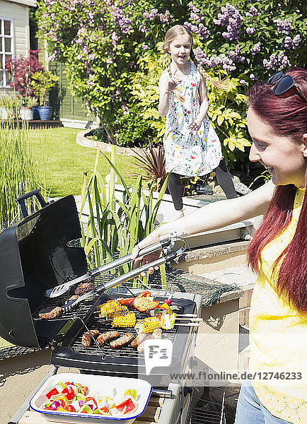 Mother and daughter barbecuing at grill in sunny backyard