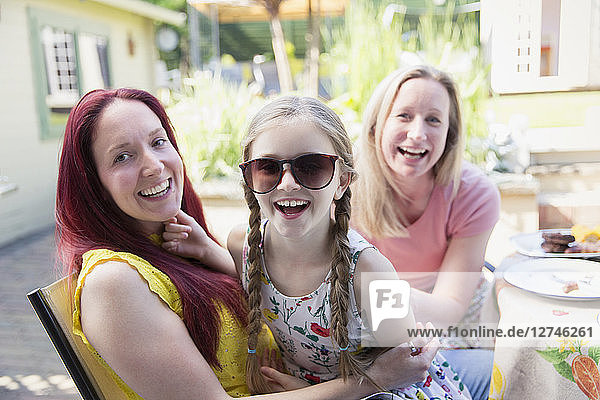 Portrait happy lesbian couple and daughter with sunglasses on patio