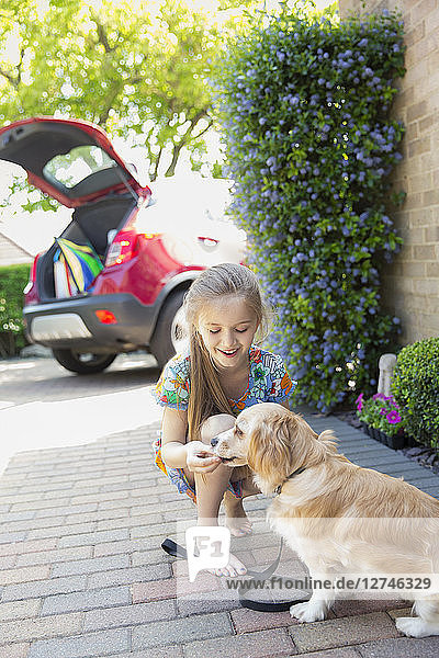 Girl giving treat to dog in driveway