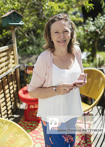 Portrait confident senior woman using smart phone on sunny patio
