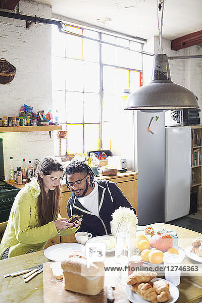 Young couple with smart phone enjoying breakfast in apartment kitchen
