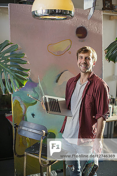 Porträt männlicher Künstler mit Laptop an großem Gemälde
