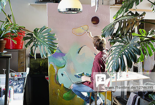 Männlicher Künstler malt auf großer Leinwand in einer Wohnung
