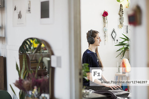 Gelassene junge Frau meditiert mit Kopfhörern in einer Wohnung