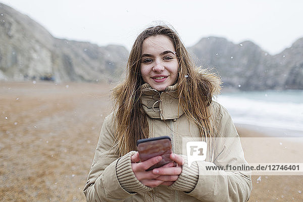 Portrait smiling teenage girl texting with smart phone on snowy winter beach