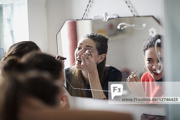 Young women friends getting ready  applying makeup in bathroom mirror