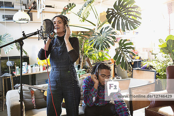 Junger Mann und Frau nehmen in einer Wohnung Musik auf und singen in ein Mikrofon