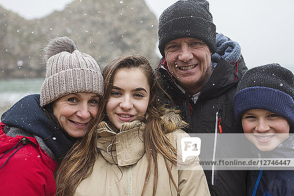 Schnee fällt über eine lächelnde Familie,  die in warmer Kleidung posiert
