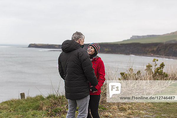 Ehepaar im Gespräch auf einer Klippe mit Blick auf das Meer