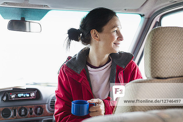 Lächelnde Frau trinkt Kaffee im Wohnmobil