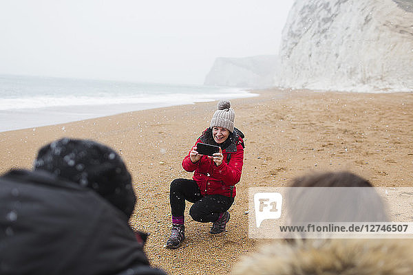 Mother with camera phone photographing kids on snowy winter beach