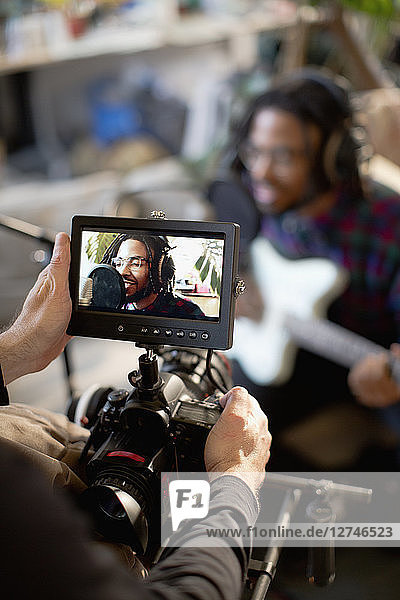 Videofilmer filmt jungen männlichen Musiker beim Singen und Gitarrenspielen