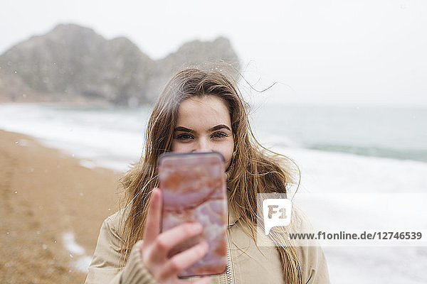 Teenager-Mädchen mit Kamera-Handy unter Selfie auf Winter Ozean Strand