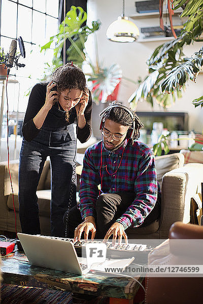 Young man and woman recording music  playing keyboard piano in apartment