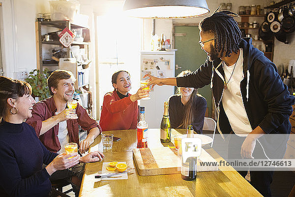 Young adult friends enjoying cocktails at apartment kitchen table