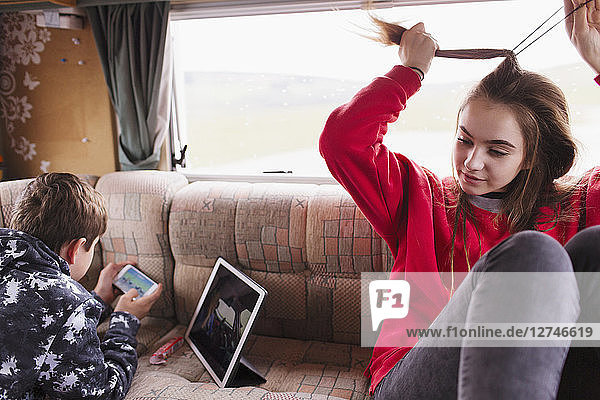 Bruder und Schwester im Teenageralter entspannen sich im Wohnmobil und benutzen Tablet und Smartphone