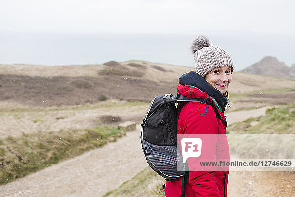 Portrait smiling woman in warm clothing with backpack hiking on remote path