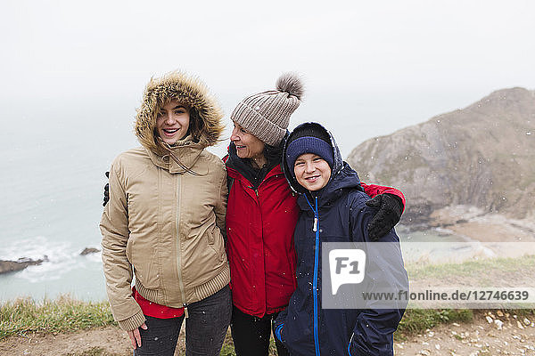 Portrait happy family in warm clothing standing on cliff overlooking ocean
