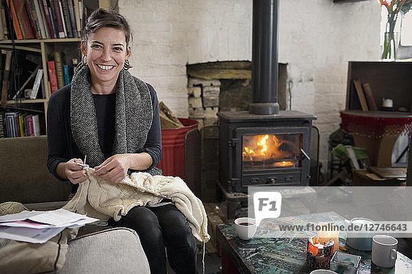 Porträt einer lächelnden  selbstbewussten Frau  die am Kamin im Wohnzimmer strickt