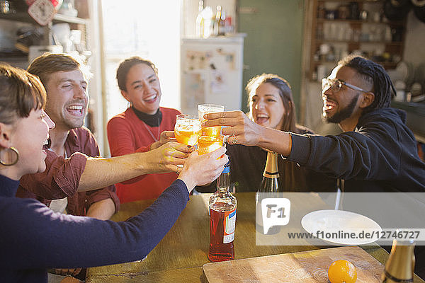 Young adult friends toasting cocktails at apartment kitchen table