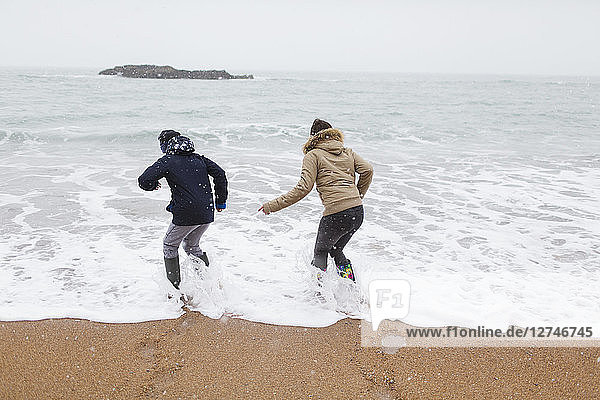Verspielter Teenager-Bruder und Tochter spielen in der winterlichen Meeresbrandung