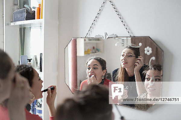 Young women friends getting ready  applying makeup in bathroom mirror