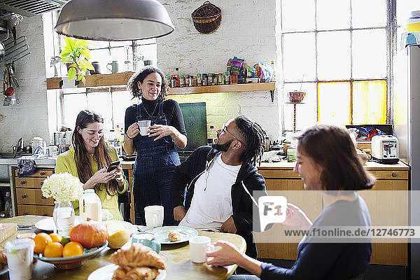 Young adult roommate friends talking at breakfast table in apartment