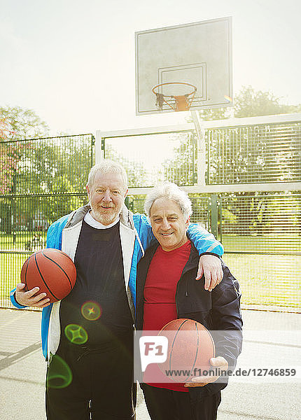 Portrait confident active senior men friends playing basketball in sunny park