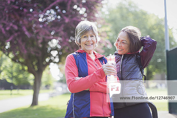 Portrait confident active senior female runner friends drinking water in park