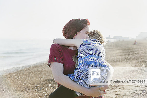 Affectionate mother holding daughter on sunny beach