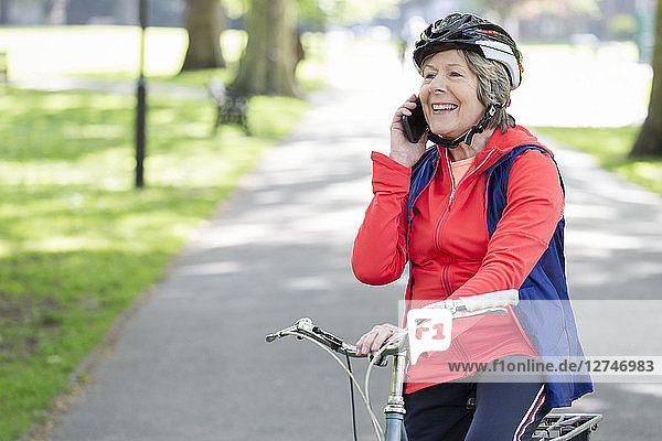 Active senior woman talking on cell phone on bike in park
