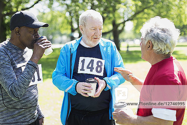 Active senior men friends finishing sports race and drinking coffee in sunny park