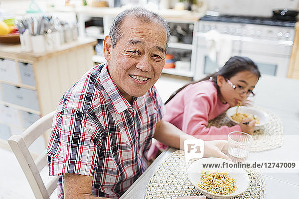 Portrait smiling grandfather eating noodles with granddaughter at table