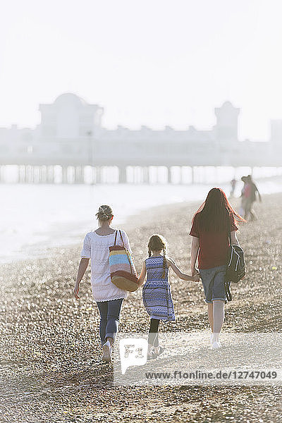 Lesbian couple and daughter holding hands on sunny beach