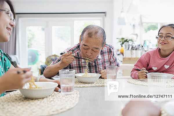 Multi-generation family eating noodles with chopsticks at table
