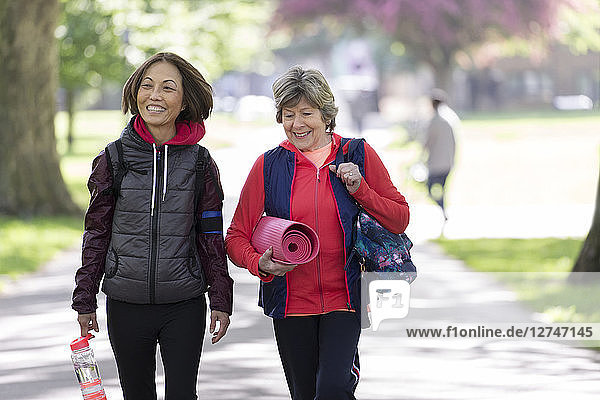 Active senior women friends with yoga mat walking in park