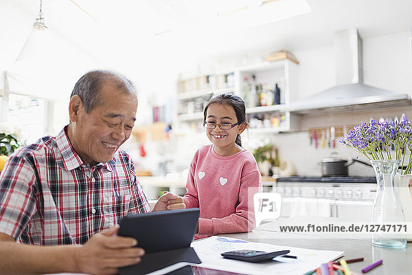 Grandfather and granddaughter using digital tablet in kitchen