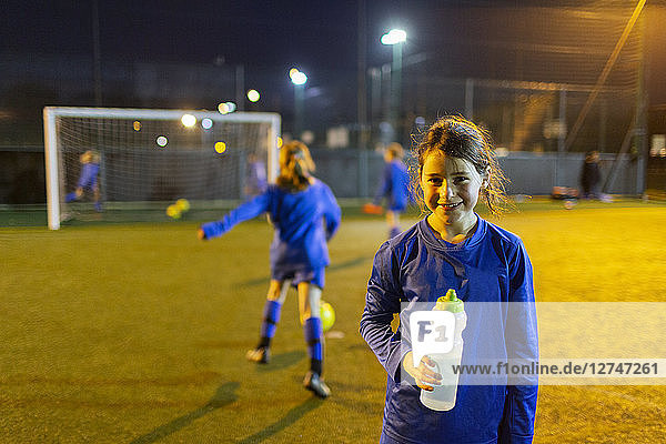 Porträt lächelndes Mädchen Fußballspieler trinken Wasser auf dem Feld in der Nacht