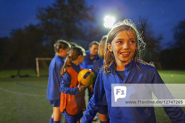 Lächelndes Mädchen spielt Fußball auf einem Feld bei Nacht
