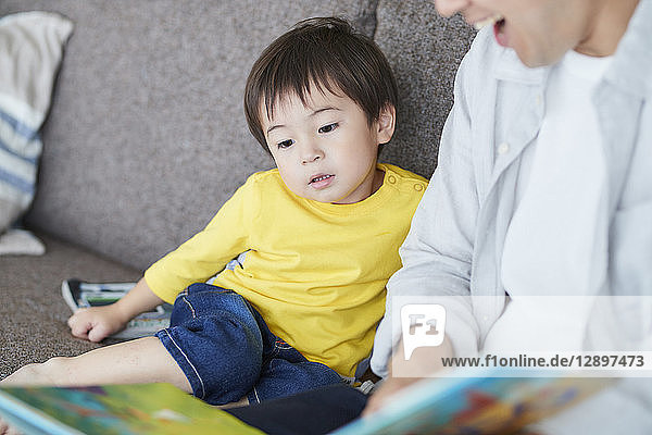 Japanischer Vater und Kind lesen auf dem Sofa