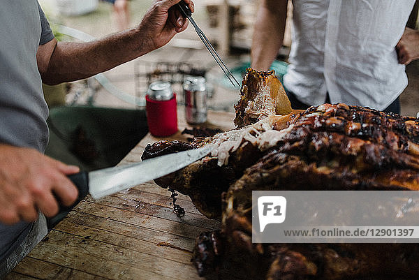 Man slicing hog roast on table  cropped